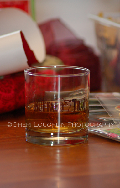 Buffalo Trace Bourbon in Buffalo Trace glass on the rocks, holiday wrapping paper in the background. - photo by Mixologist Cheri Loughlin, The Intoxicologist